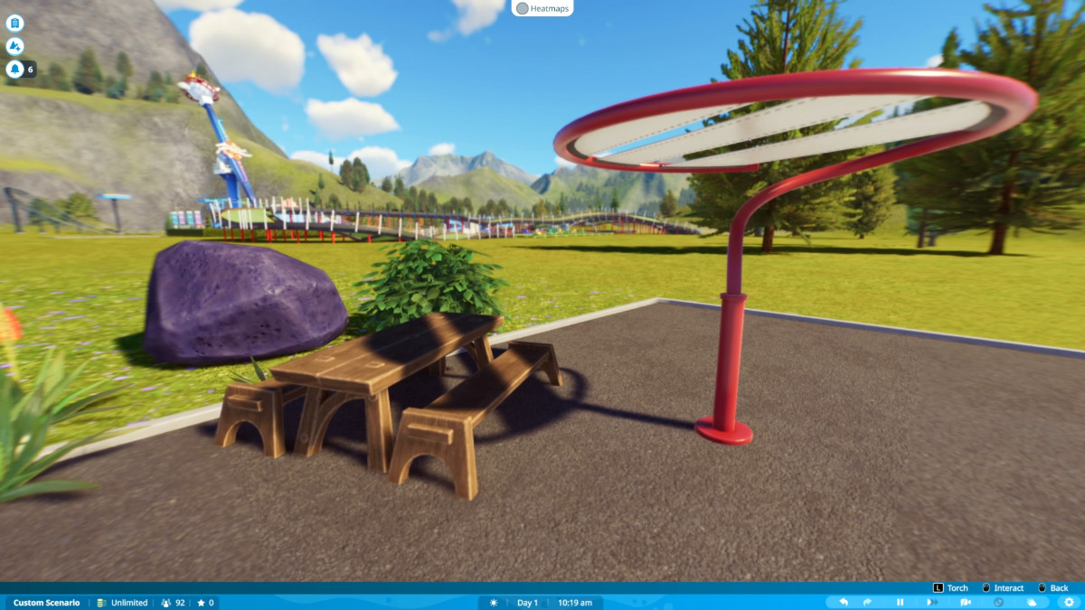 A first-person view of a bench surrounded by scenery with a theme park in the background in Planet Coaster 2